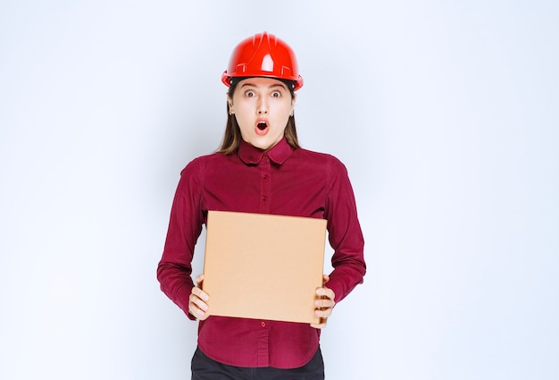 흰색 바탕에 판지 상자를 들고 빨간 헬멧에 여성 엔지니어의 사진.