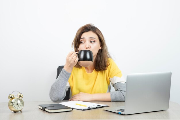 机に座ってマグカップを持っている女性サラリーマンの写真。高品質の写真