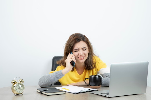 Photo of female office worker sitting at the desk and talking on mobile phone . High quality photo