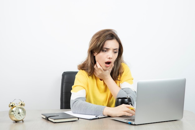 Photo of female office worker sitting at the desk with laptop and clipboard . High quality photo