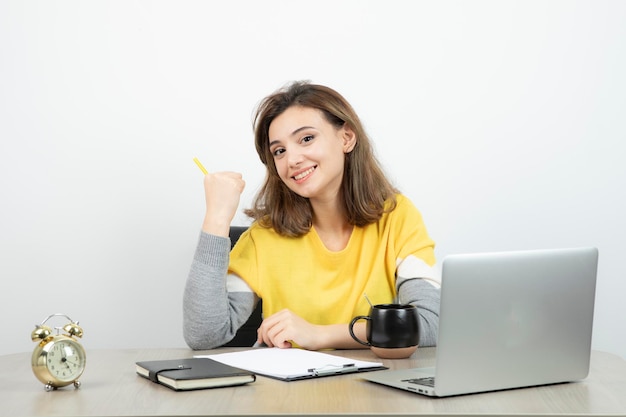 Photo of female office worker sitting at the desk with laptop and clipboard . High quality photo