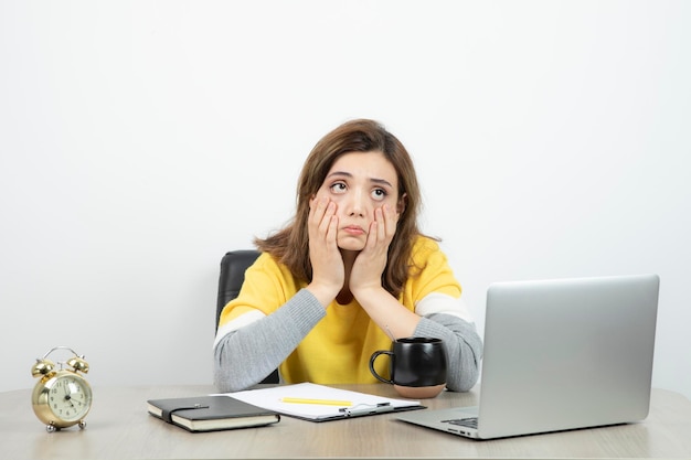 Photo of female office worker sitting at the desk with laptop and clipboard . High quality photo