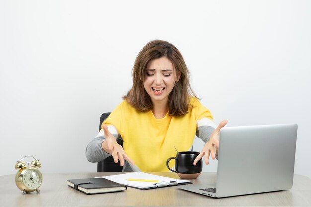 Photo of female office worker sitting at the desk with laptop and clipboard . High quality photo