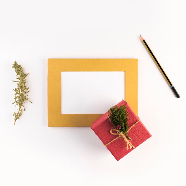 Photo frame near present box, pencil and coniferous twig