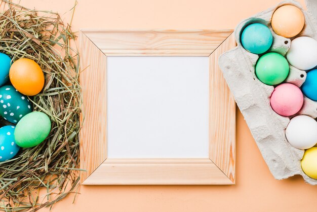 Photo frame near set of bright Easter eggs in nest and container