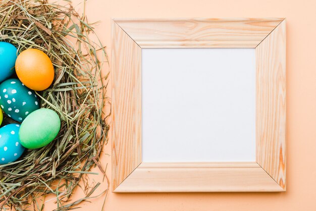 Photo frame near set of bright Easter eggs in nest