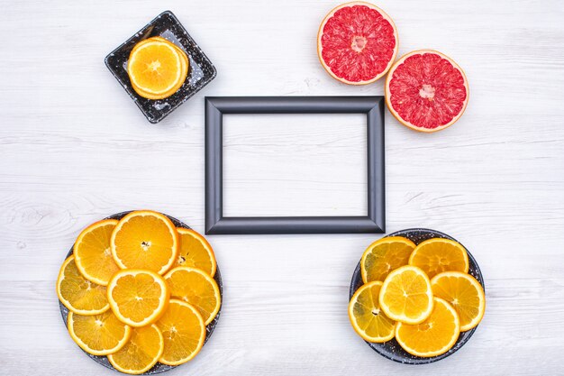 Фоторамка окружена апельсиновыми ломтиками в черной тарелке и двумя кусочками грейпфрута на деревянной поверхности