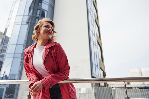 Photo from below. Adult pretty woman in warm red coat have walk in the city at her weekends time