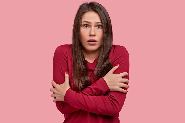 Photo of frustrated woman crosses hands over chest, trembles from fear, scared of horrified scene, wears red shirt