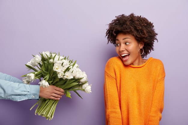嬉しいアフロアメリカの若い女性の写真は、男性が持っている花の花束を喜んで見ています