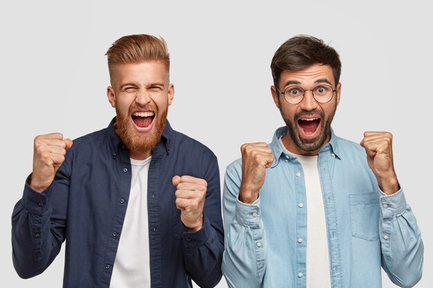 Photo of glad bearded men comapnions raise clenched fists, feel optimism