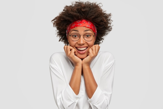 Photo of glad dark skinned girl holds chin with both hands