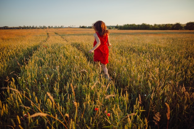 黄金の夏の畑に立っている赤いドレスのゴージャスな女性の写真