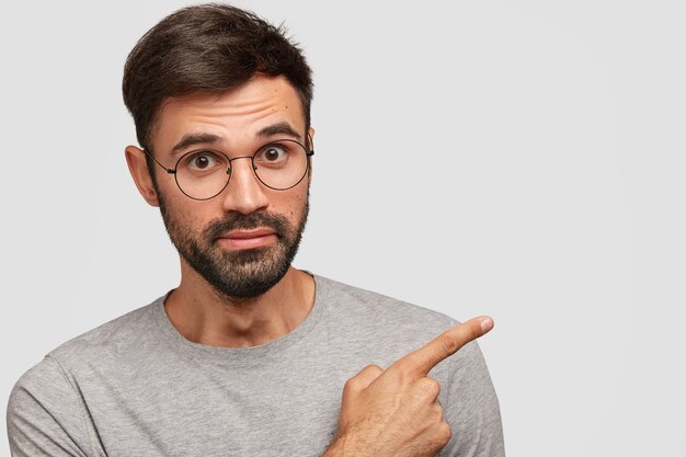 Photo of handsome European male with thick beard, points with fore finger aside