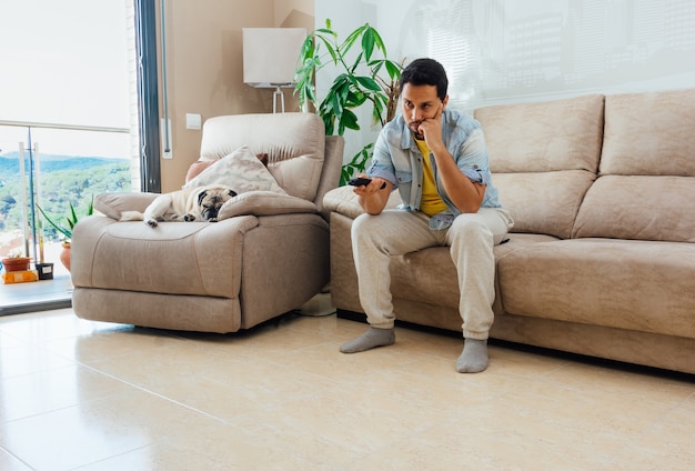 Photo of a handsome Hispanic man sitting on a sofa and watching TV