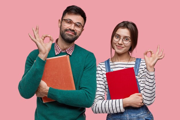Photo of handsome male student and his female groupmate demonstrates okay gesture, agree with something
