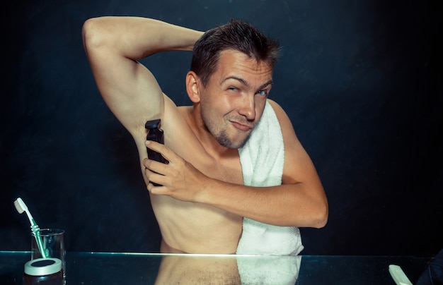 Free photo photo of handsome man shaving his armpit. the young man in bedroom sitting in front of the mirror at home