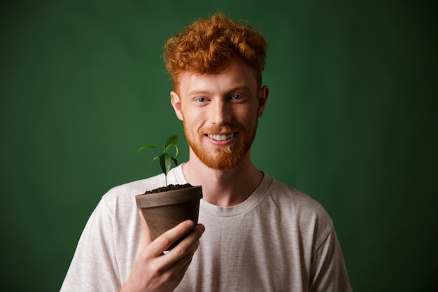 Photo of handsome redhead bearded young man, holding potted plant
