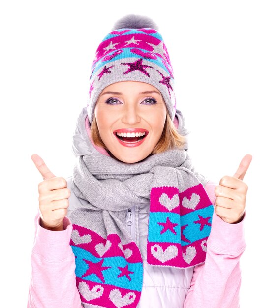 Photo of a happy adult girl in winter clothes with bright positive emotions shows thumbs up sign isolated on white