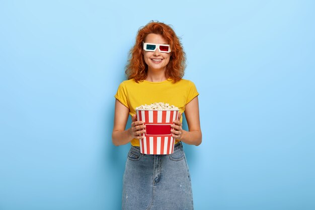 Photo of happy ginger charming girl holds bucket with popcorn