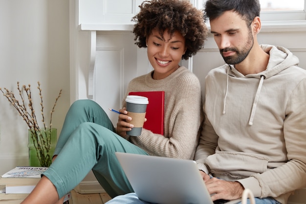 Photo of happy multiracial male and female friends watch video on laptop computer, have leisure time at home.