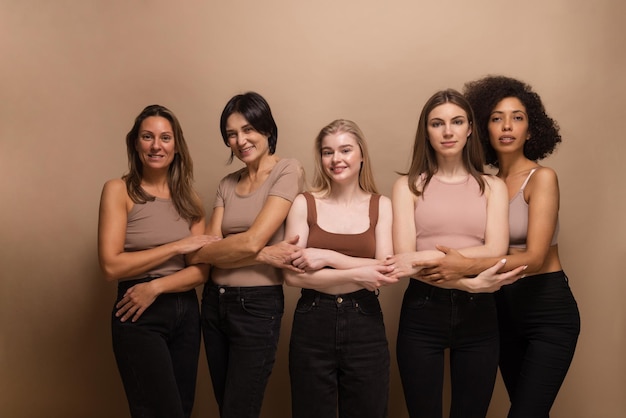 Free photo photo of interracial young and adult women in tops jeans stand on beige background with crossed arms