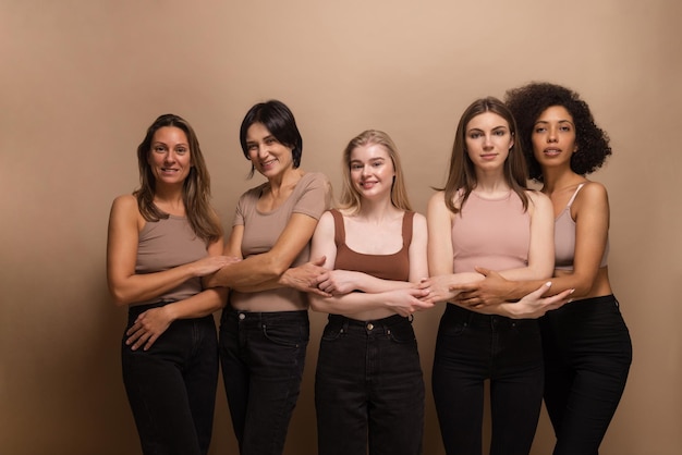 Free photo photo of interracial young and adult women in tops jeans stand on beige background with crossed arms