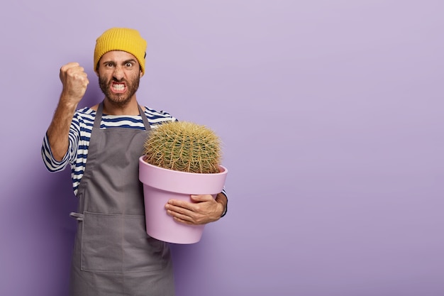 Photo of irritated European male florist clenches fist with anger