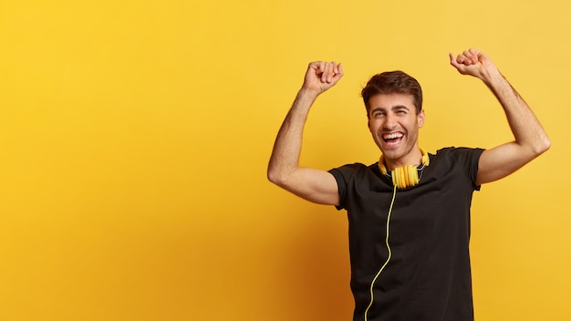 Photo of joyful Caucasian man raises hands with triumph