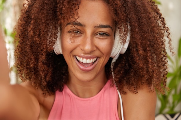 Photo of joyful dark skinned girl listens music with modern stereo headpones