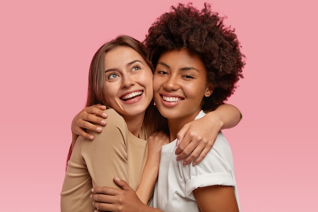 Photo of joyful two women embrace and smile positively, have dreamy expressions, demonstrate truthful feelings