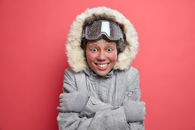 Free photo photo of joyful woman with red cheeks covered by hoarfrost embraces herself wears warm thermo jacket.