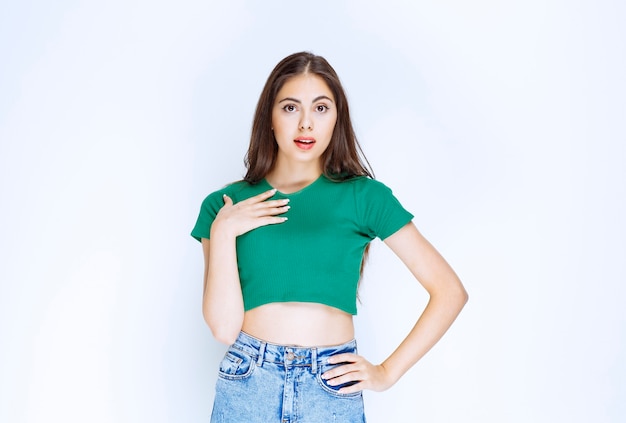 Photo of a lovely girl model standing and looking at camera against white wall.