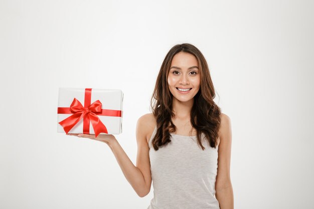 Photo of lovely woman holding gift-wrapped box with red bow being excited and surprised to get holiday present, isolated over white
