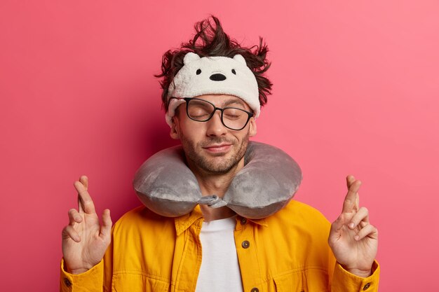 Photo of male with crossed fingers, believes in good luck with travel pillow