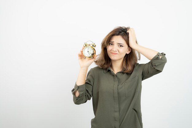Photo of morning girl holding alarm clock over white wall. High quality photo