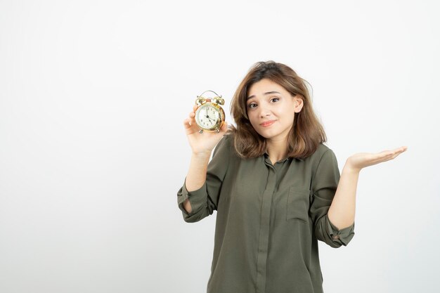 Photo of morning girl holding alarm clock over white wall. High quality photo