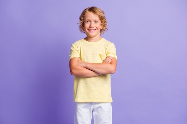 Фотография очаровательного позитивного мальчика с перекрещенными руками смотрит в камеру с зубастой улыбкой в повседневной одежде, изолированной на фиолетовом фоне