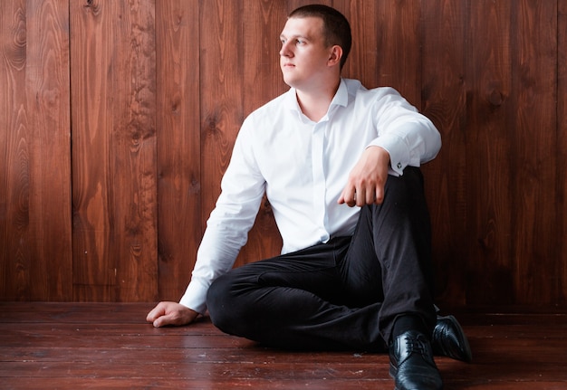 ズボンとシャツの男の写真は床に座って 木製の壁の背景にポーズ プレミアム写真