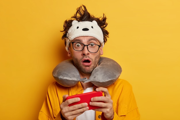 Бесплатное фото Фотография шокированного смущенного человека, увлекающегося современными технологиями, играющего в видеоигры на смартфоне во время путешествия в самолете