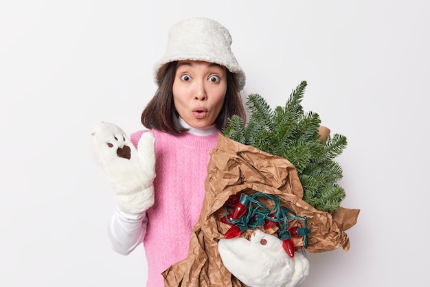 기절 한 여성의 사진은 종이에 싸인 상록 가문비 나무 가지와 흰 벽에 고립 된 크리스마스 시장에서 화환 반환을 들고 겨울 옷을 입고 멍하니 숨을 멈 춥니 다.