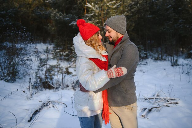 젊은 매력적인 커플의 사진 행복한 긍정적인 미소가 서로를 바라보며 함께 시간을 즐깁니다. 숲속 겨울 사랑 이야기