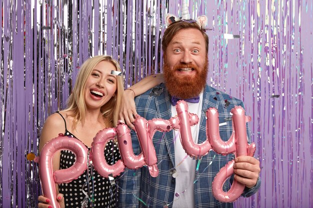 Photo of optimistic husband and wife hold pink letter shaped balloon