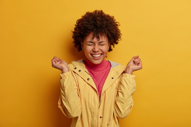 Photo of overemotive woman watches comedy, laughs happily with clenched fists, feels entertained and has fun, keeps eyes closed, cheers excellent score