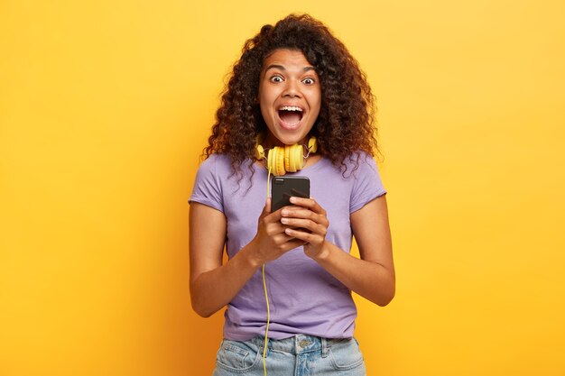 Photo of overemotive young female with afro hairstyle posing against the yellow wall