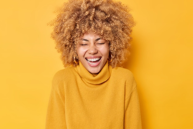 大喜びのヨーロッパの女性の写真は心から笑う広く明るい気分は目を閉じたままにします黄色の背景の上に分離されたカジュアルな暖かいジャンパーを着ています本物の幸せな感情の概念