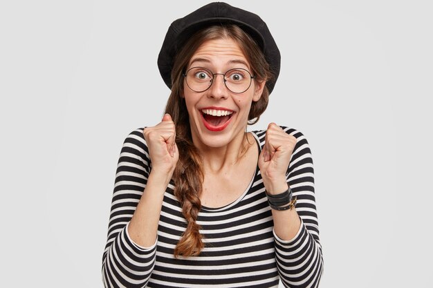 Photo of overjoyed French female clenches fists and looks joyfully at camera