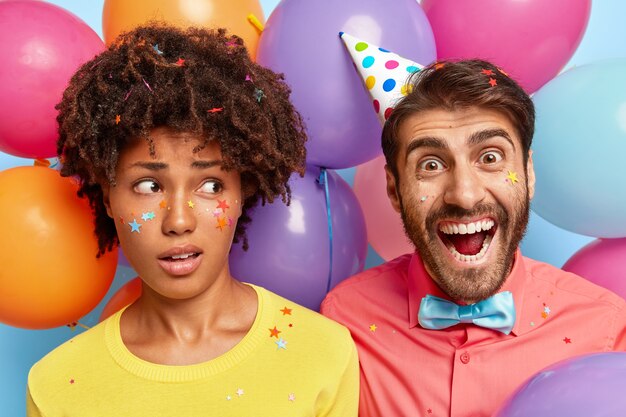 Photo of overjoyed young couple posing surrounded by birthday colorful balloons