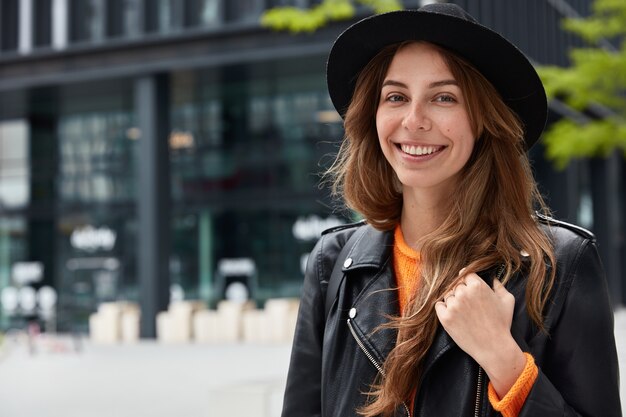 Photo of pleasant looking young female tourist poses with happy smile at street