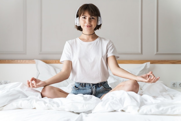Photo of a pleased concentrated beautiful young lady indoors at home listening music with headphones meditate.